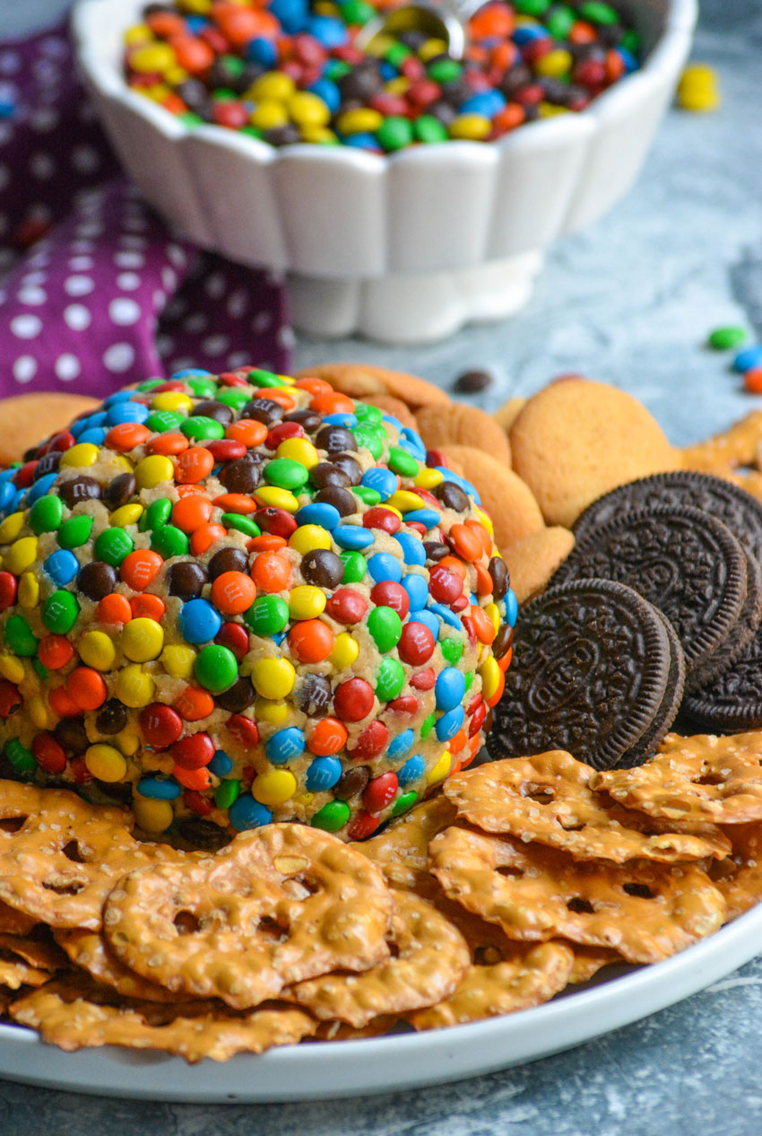 monster cookie cheeseball surrounded by cookies and pretzels on a white plate