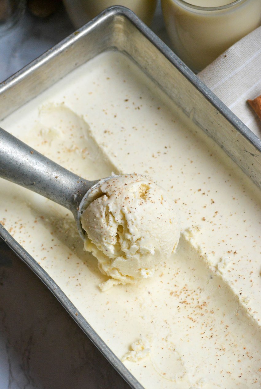 a silver ice cream scoop scooping eggnog ice cream out of a metal loaf pan
