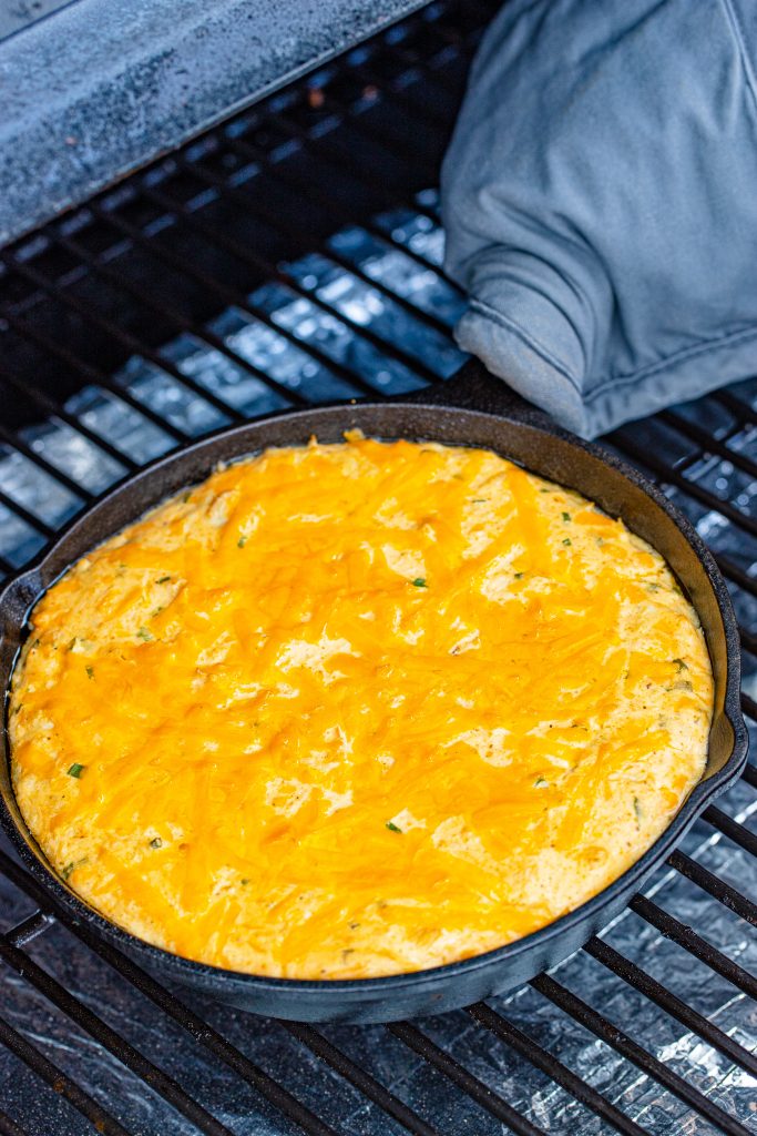 a cast iron skillet filled with smoked crab dip sitting on the grate of a smoker grill