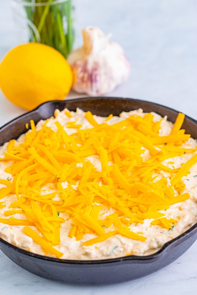a cast iron skillet filled with smoked crab dip mixture and topped with shredded cheddar cheese