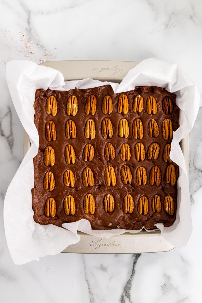 chocolate cheese fudge topped with whole pecans in a parchment paper lined square baking dish
