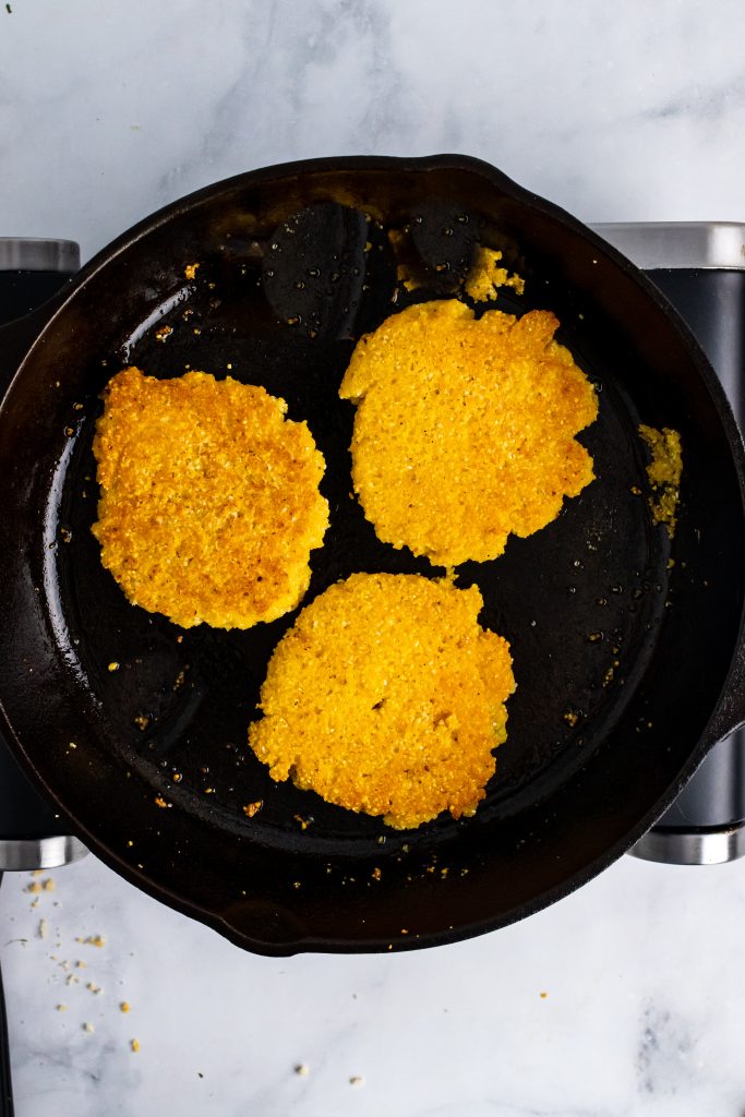 three fried hot water cornbread cakes in a cast iron skillet