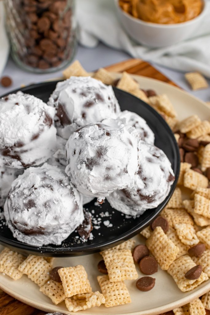 a black plate with a pile of powdered sugar covered puppy chow truffles on it