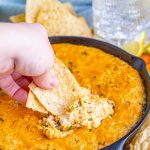 a hand scooping smoked crab dip out of a black skillet with tortilla chips