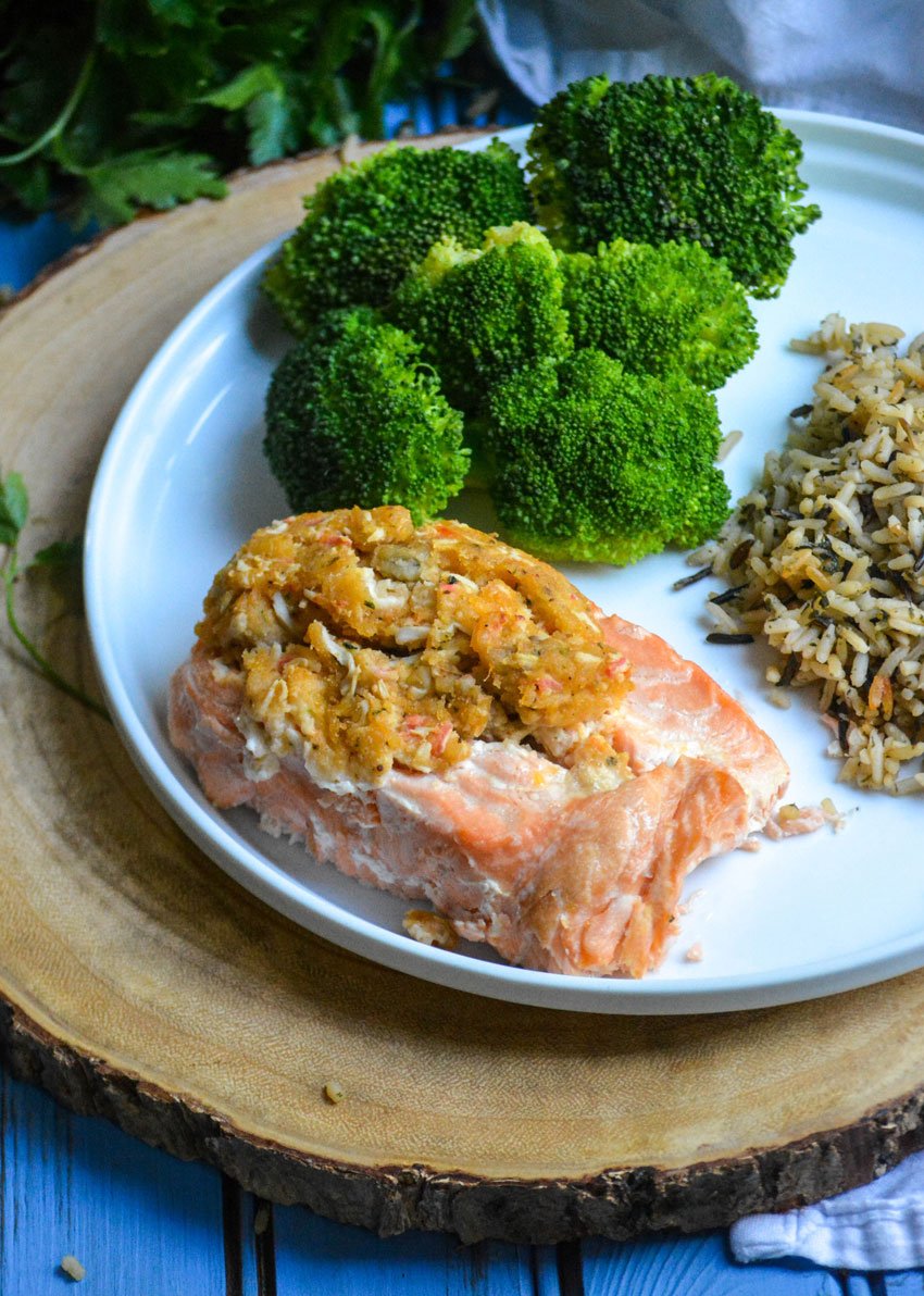 seafood stuffed salmon arranged on a white plate with steamed broccoli and cooked wild rice