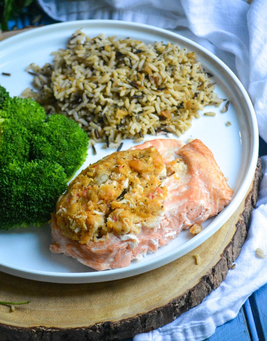 seafood stuffed salmon arranged on a white plate with steamed broccoli and cooked wild rice