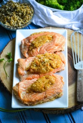 three crab stuffed salmon fillets in a row on a white serving platter