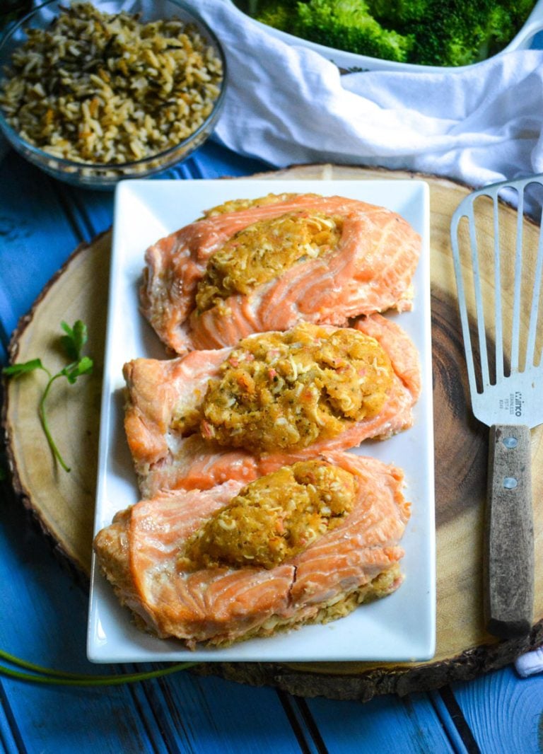 three crab stuffed salmon fillets in a row on a white serving platter