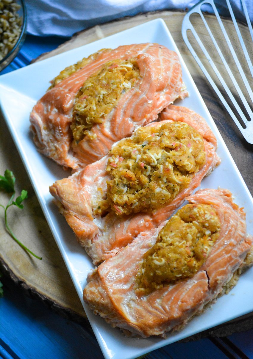 three crab stuffed salmon fillets in a row on a white serving platter