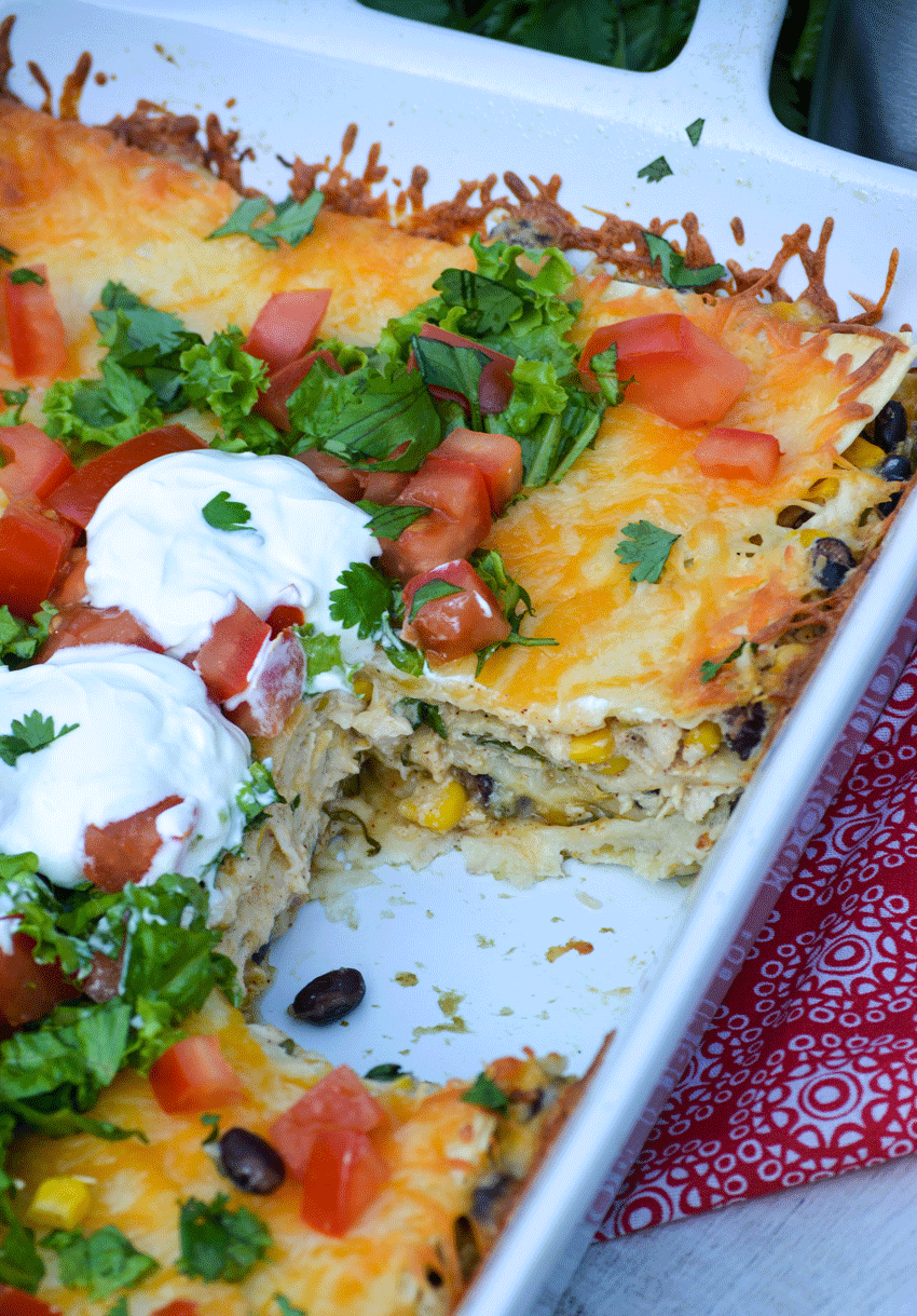 Mexican lasagna in a white casserole dish with a piece cut out and removed