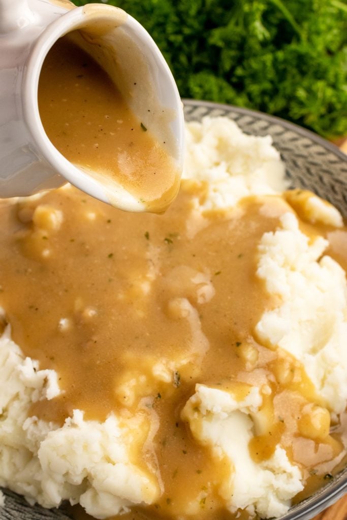 easy homemade gravy being poured over mashed potatoes in a gray bowl