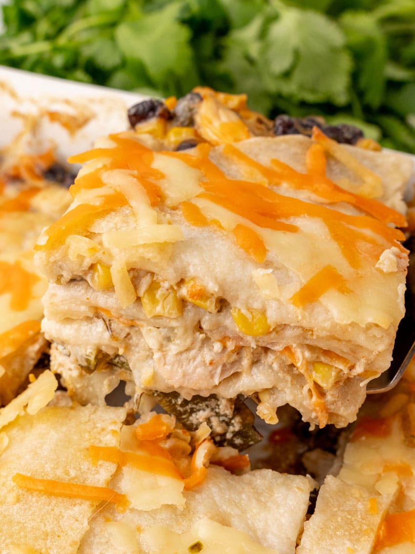 a spatula lifting up a slice of cheesy Mexican lasagna with chicken