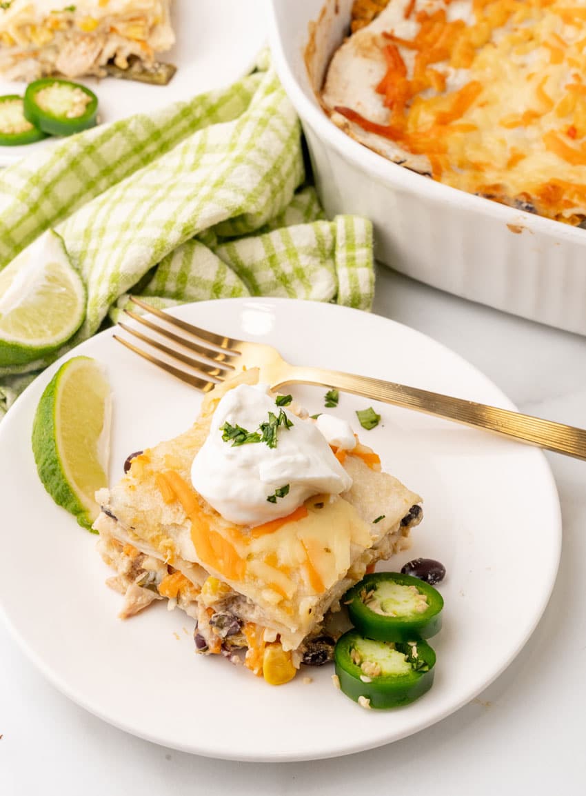 a slice of Mexican lasagna topped with a dollop of sour cream on a white plate