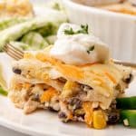 a slice of Mexican lasagna topped with a dollop of sour cream on a white plate