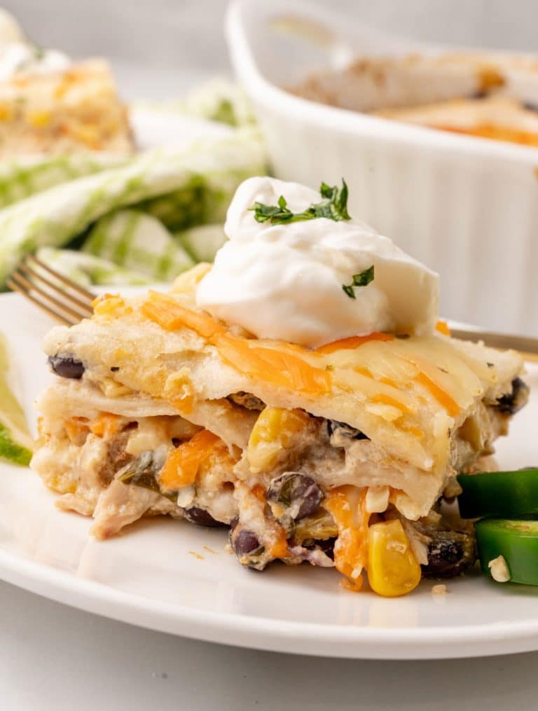 a slice of Mexican lasagna topped with a dollop of sour cream on a white plate