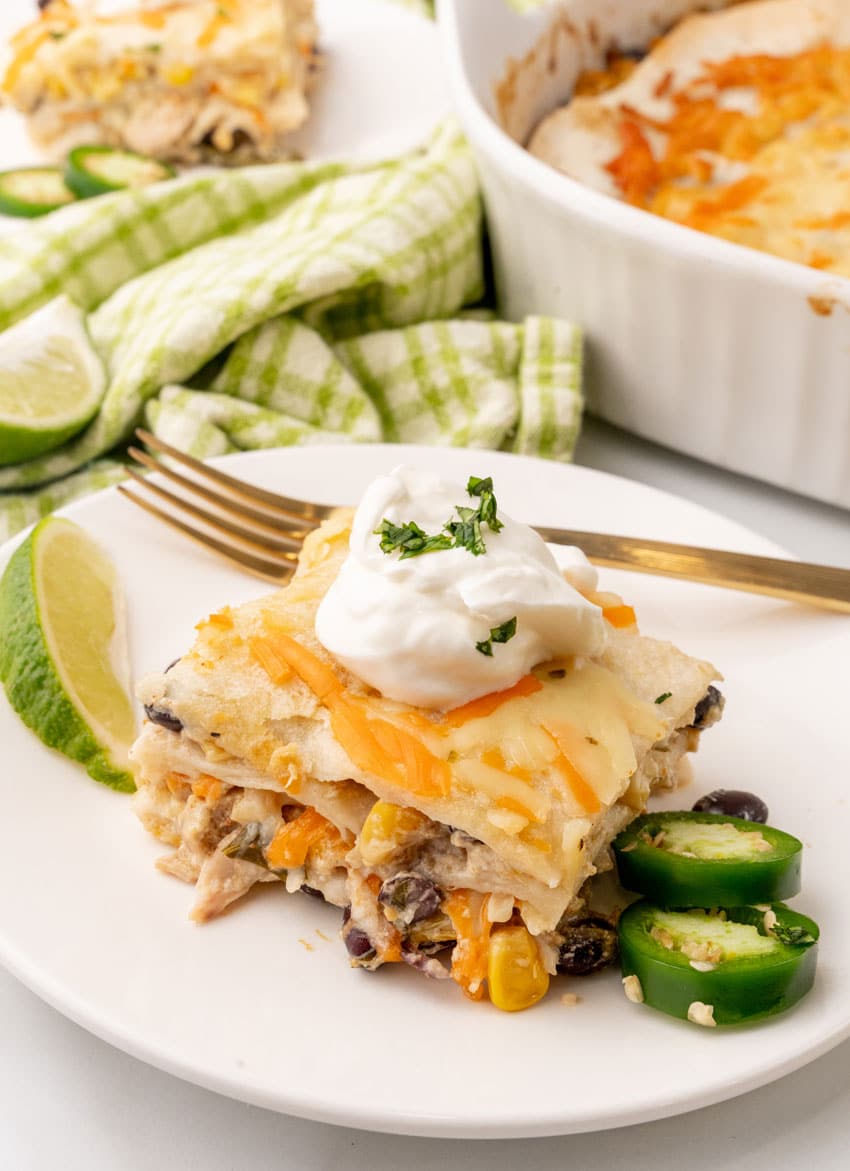 a slice of Mexican lasagna topped with a dollop of sour cream on a white plate