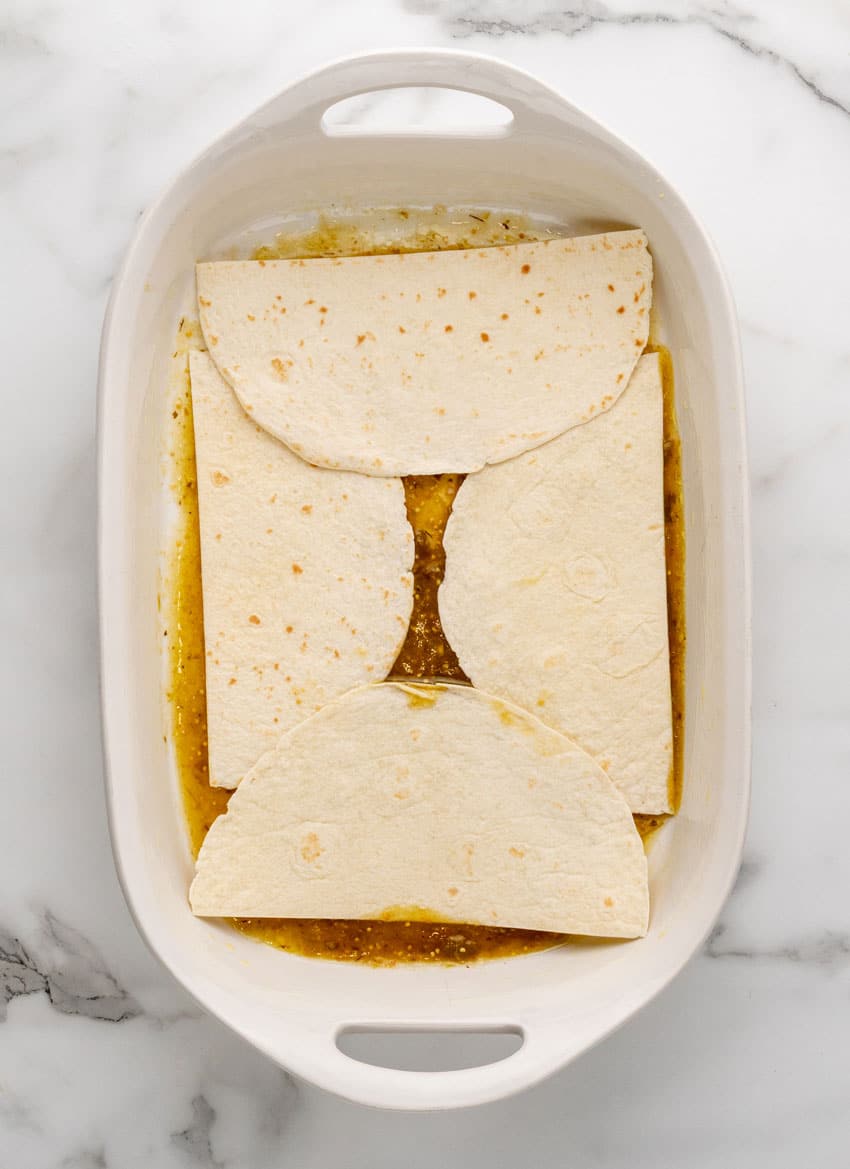 flour tortilla on top of salsa verde in a white casserole dish