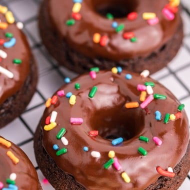 chocolate glazed chocolate donuts with sprinkles on a metal wire cooling wrack