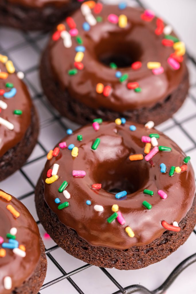 chocolate glazed chocolate donuts with sprinkles on a metal wire cooling wrack
