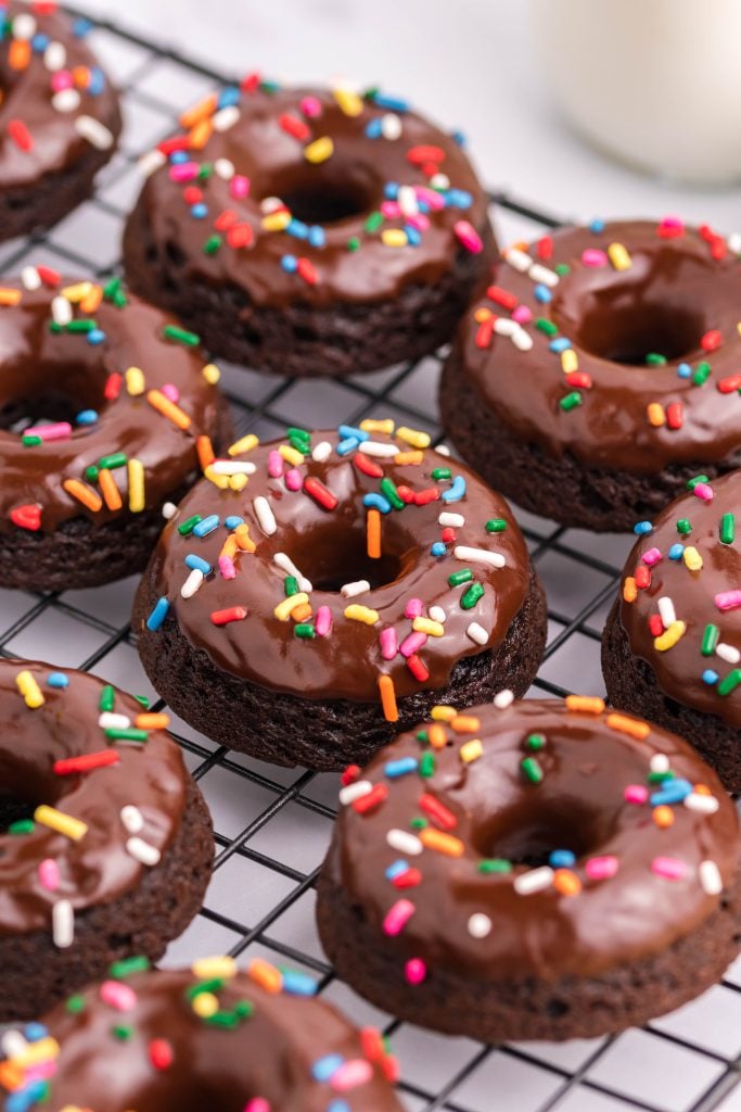 sprinkle topped double chocolate donuts on a metal cooling wrack
