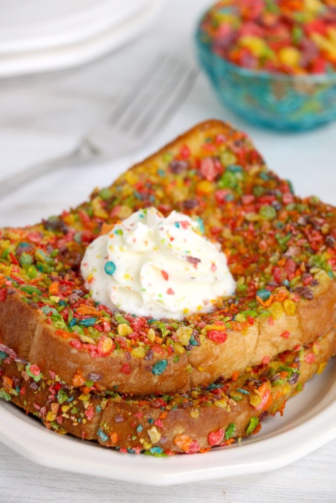 two slices of air fryer fruity pebble french toast topped with whipped cream