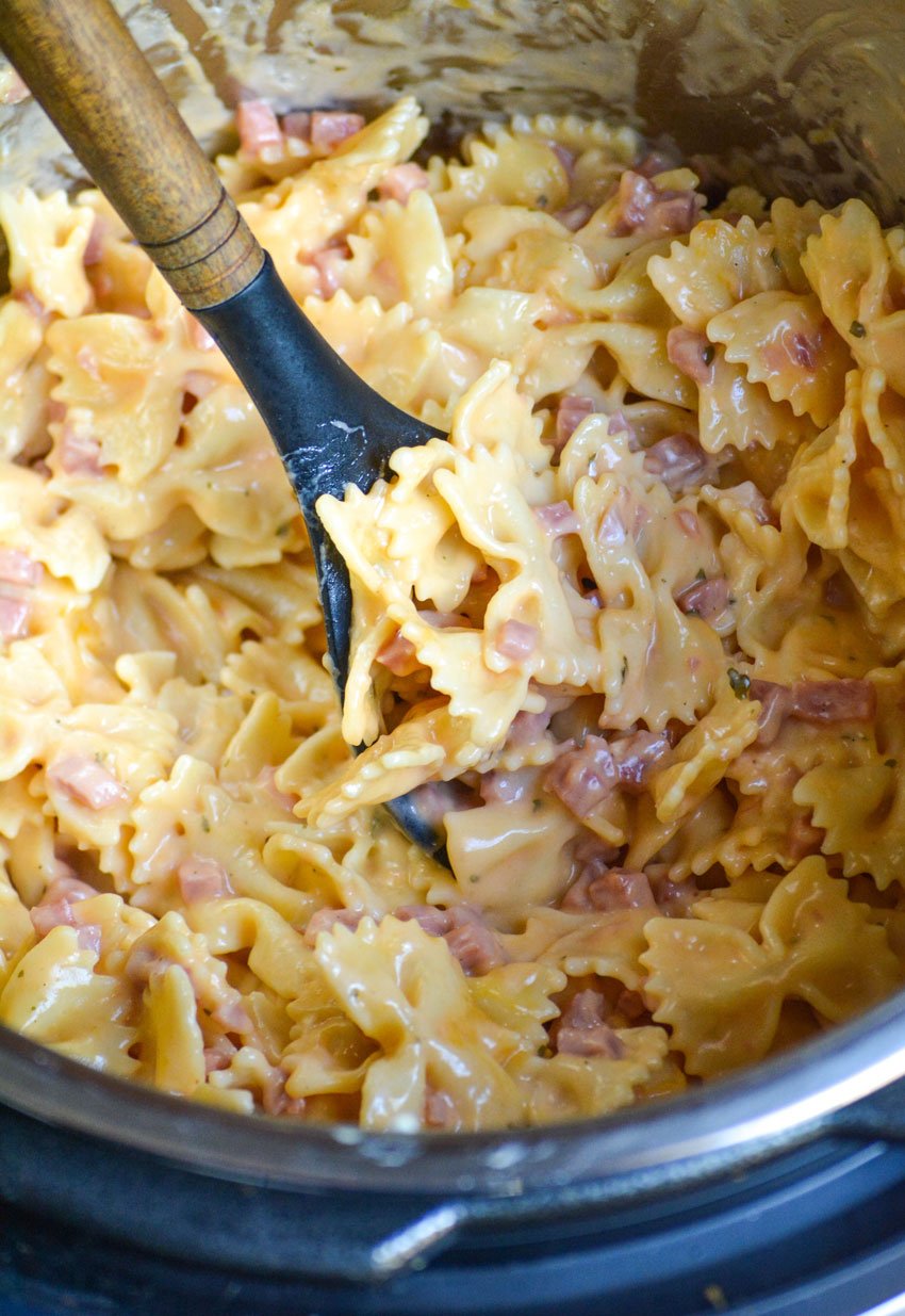 a wooden spoon stuck in an instant pot filled with cheesy ranch pasta with ham