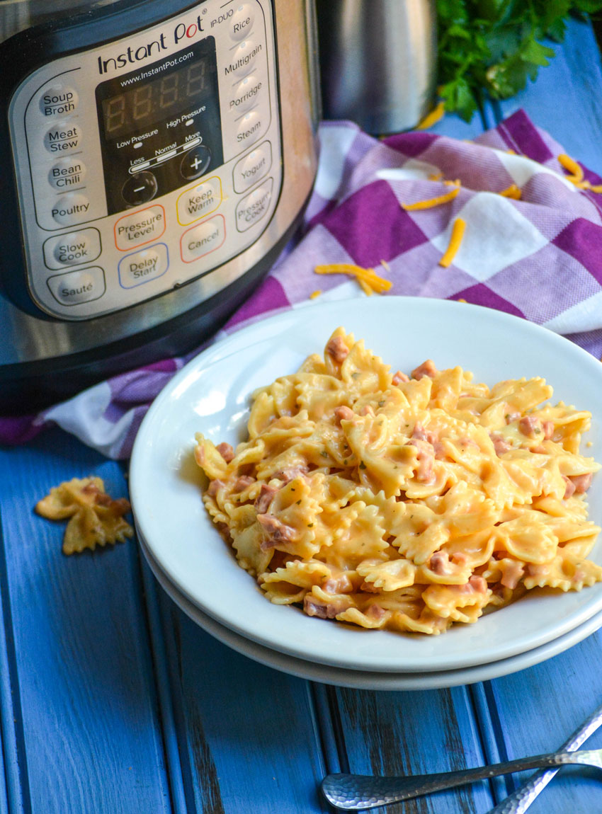 a white bowl filled with cheesy pasta and ham in front of an Instant Pot