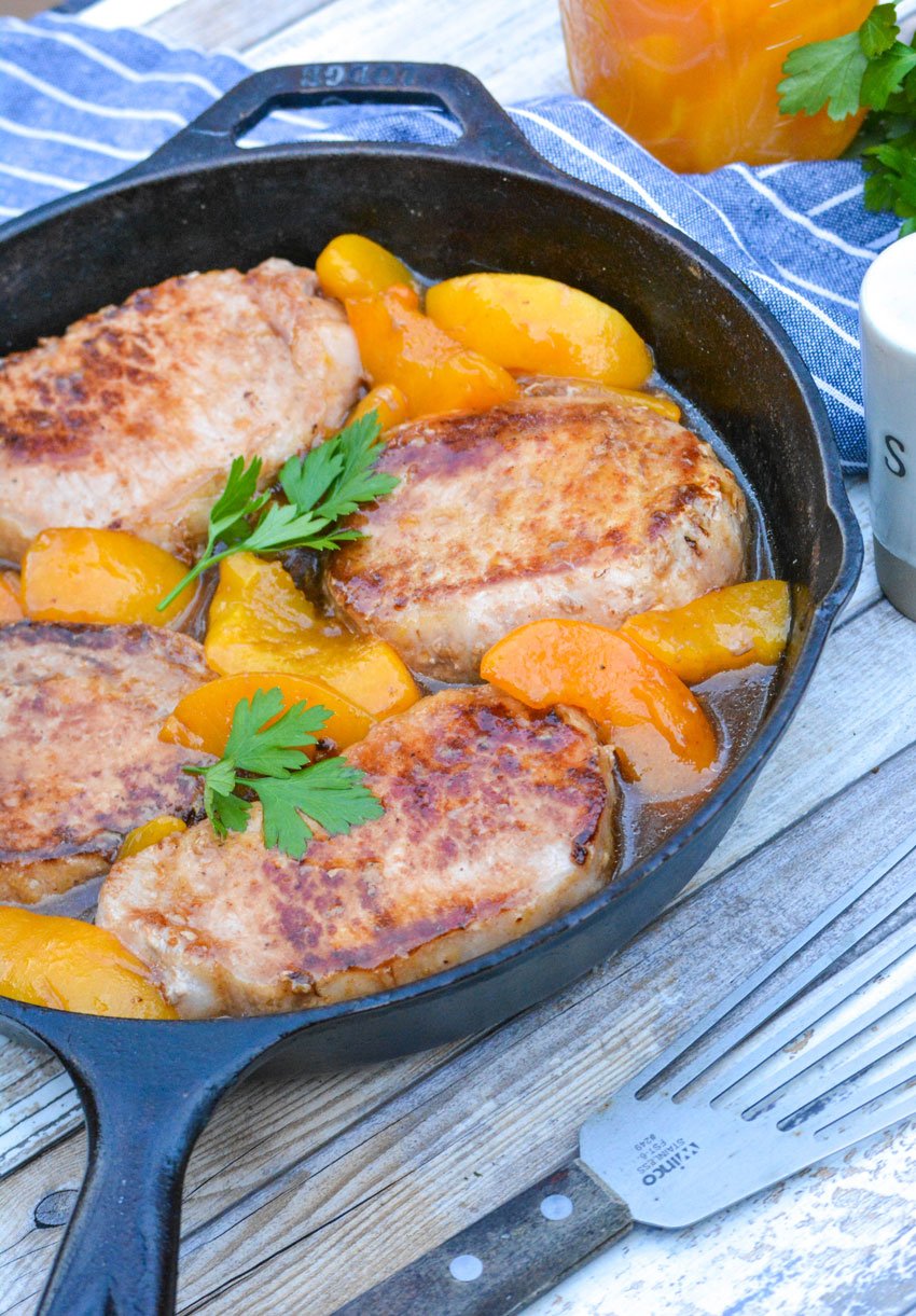 peaches and pork chops topped with fresh herbs shown in a black cast iron skillet