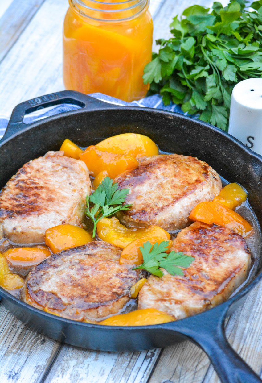 peaches and pork chops topped with fresh herbs shown in a black cast iron skillet