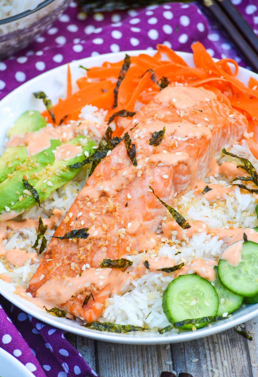 a white salmon sushi bowl topped with seaweed strips and a sriracha cream sauce