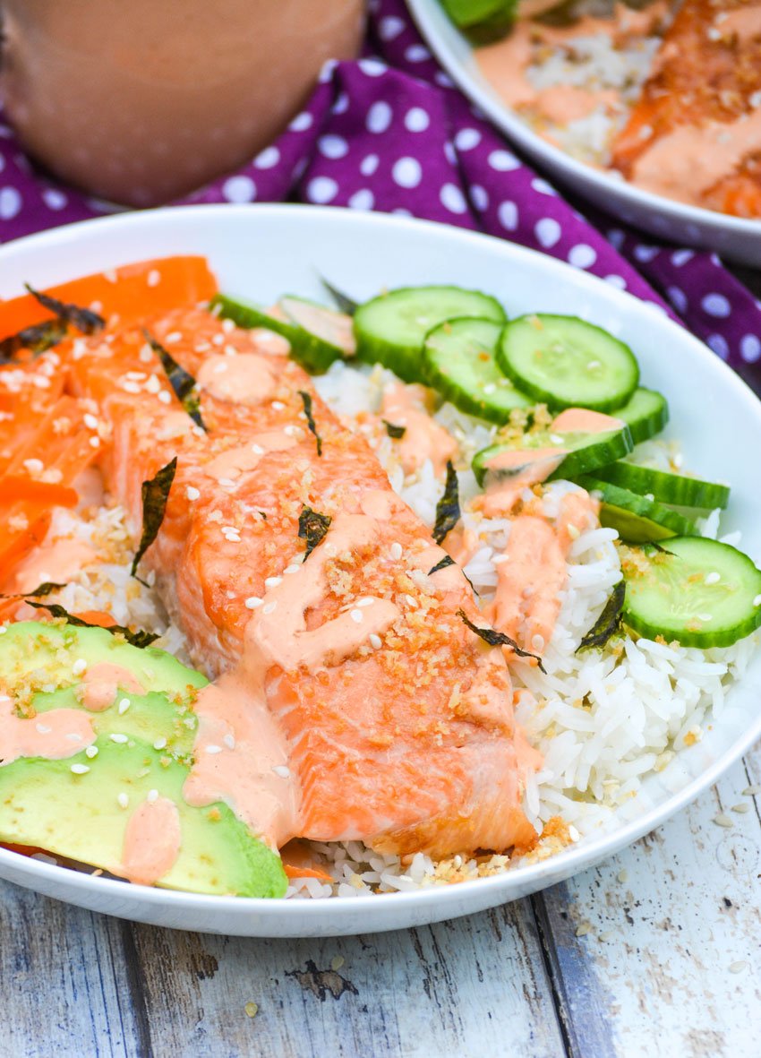 a white salmon sushi bowl topped with seaweed strips and a sriracha cream sauce
