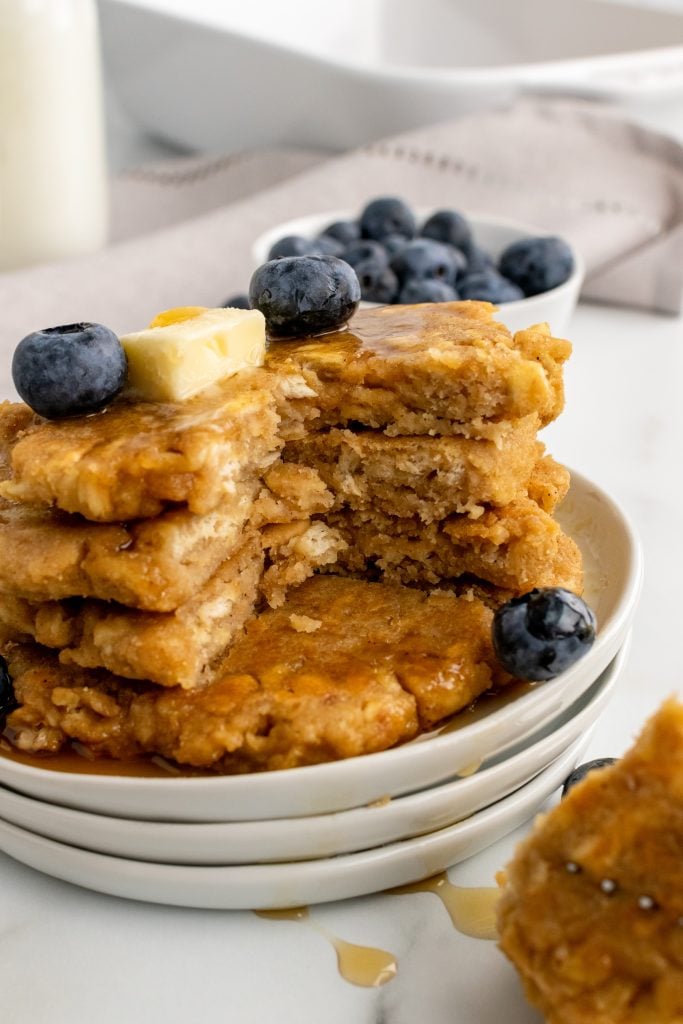 a stack of saltine cracker fritters topped with blueberries, butter, and syrup on white plates