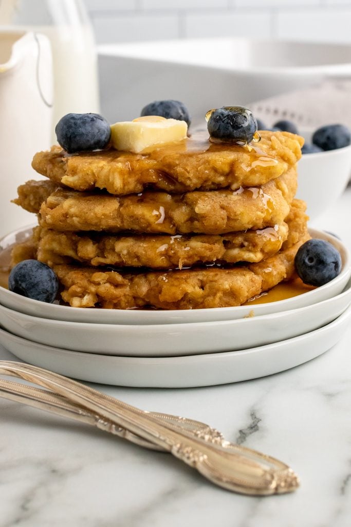 a stack of saltine cracker fritters topped with blueberries, butter, and syrup on white plates