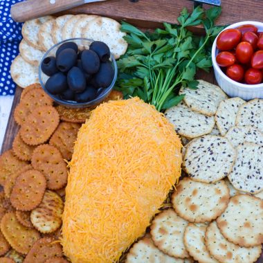 carrot cheese ball on a wooden serving tray surrounded by crackers and fresh vegetables