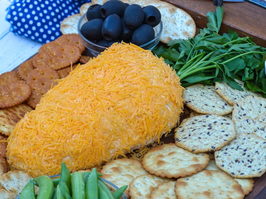 carrot shaped bacon cheddar ranch cheese ball on a wooden serving tray surrounded by fresh vegetables and assorted crackers