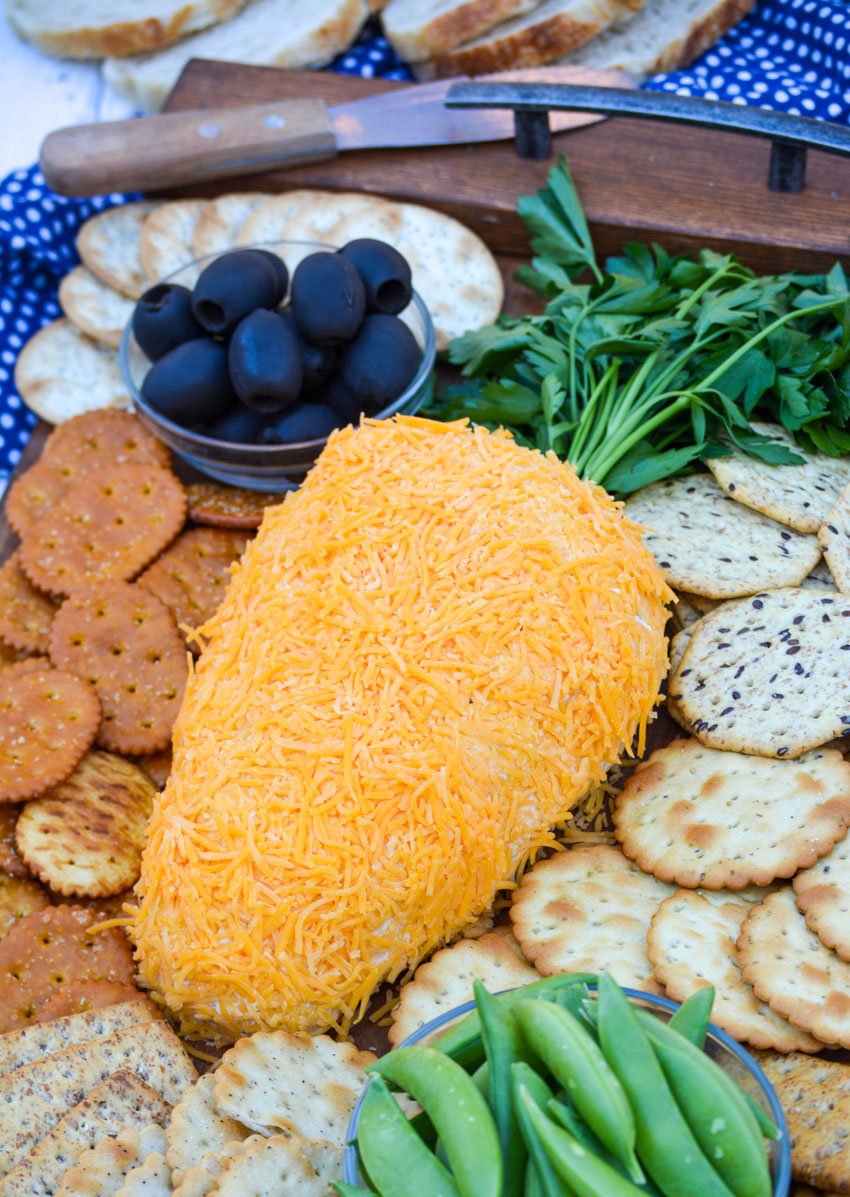 carrot cheese ball on a wooden serving tray surrounded by crackers and fresh vegetables