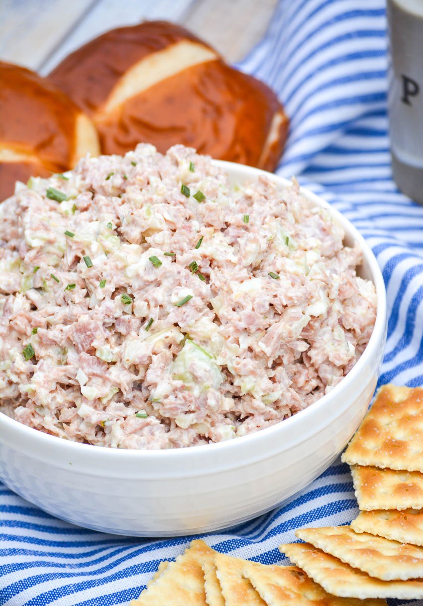 deviled ham salad in a white bowl with pretzel rolls and crackers around the outside
