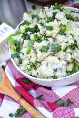 a white bowl full of colcannon topped with leafy greens and sliced green onions