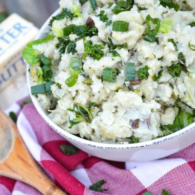 a white bowl full of colcannon topped with leafy greens and sliced green onions