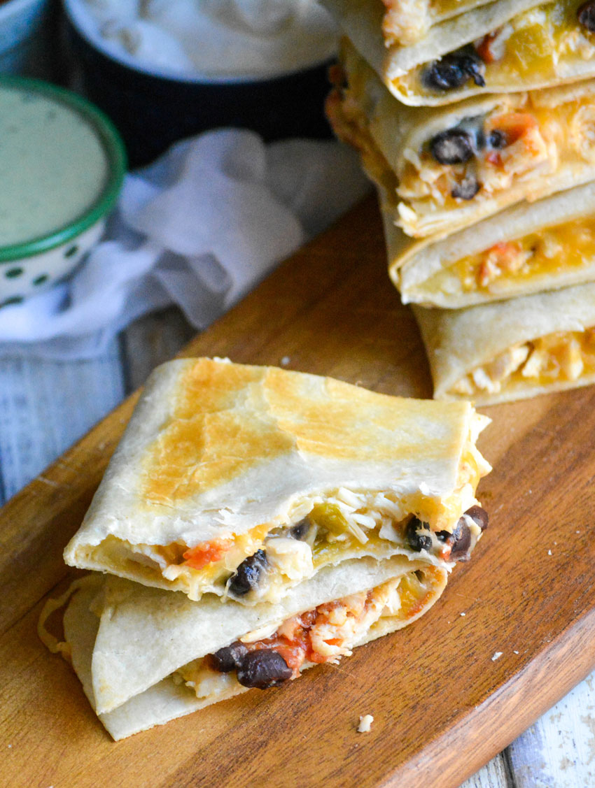 slices of sheet pan chicken quesadilla on a wooden cutting board halved to reveal the filling inside