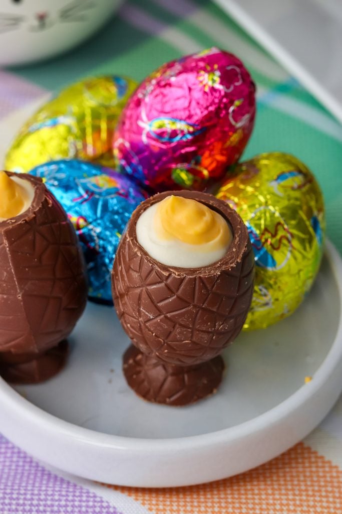 a cheesecake stuffed chocolate Easter egg on a white plate with colorful tinfoil wrapped chocolate eggs in the background