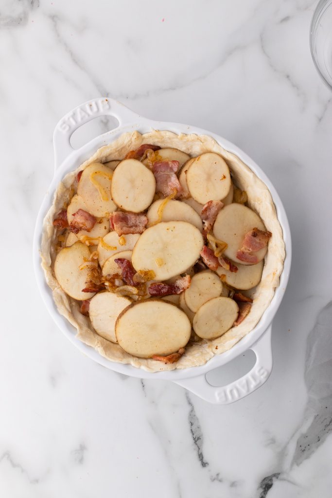 sliced potatoes and crisp bacon layered in a pie crust in a white dish