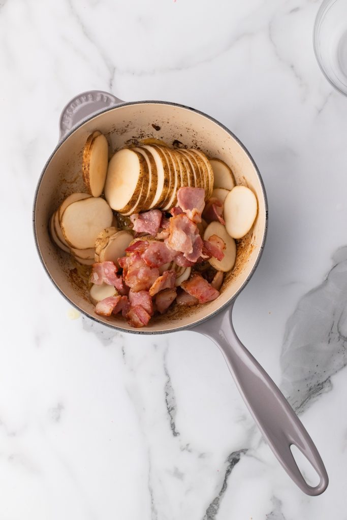 slices potatoes and cooked pieces of bacon in a gray enameled cast iron skillet