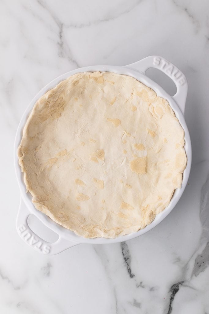 puff pastry spread out in a white pie dish to form a crust