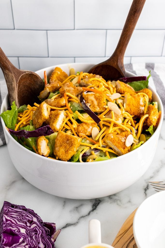 copycat applebee's oriental chicken salad served in a white salad bowl with wooden salad servers on the side