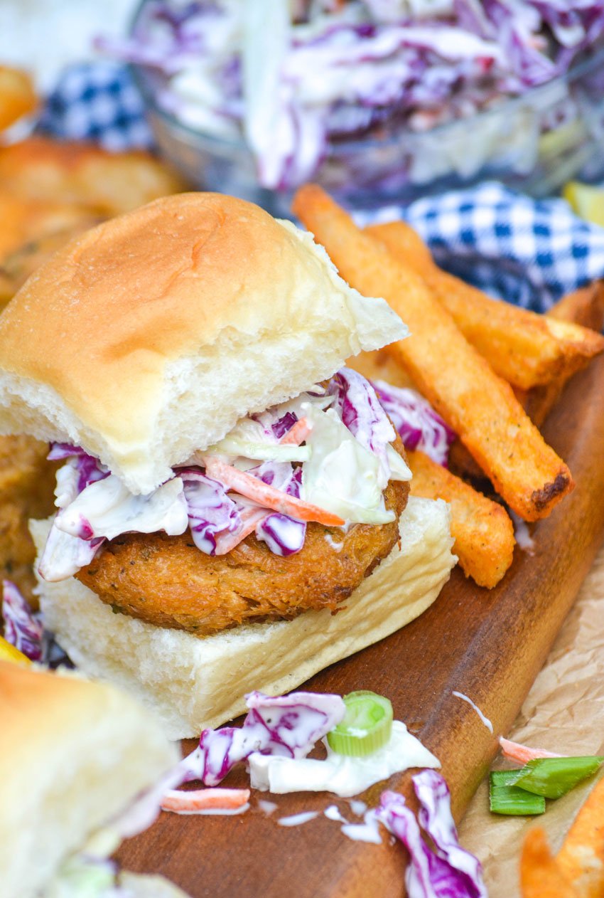close up of a creamy slaw topped crab cake slider next to seasoned fries on a wooden cutting board