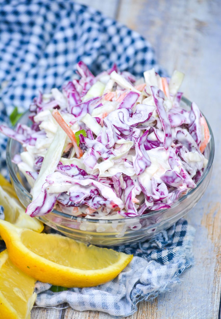 creamy tri color coleslaw in a glass bowl with lemon wedges on the side