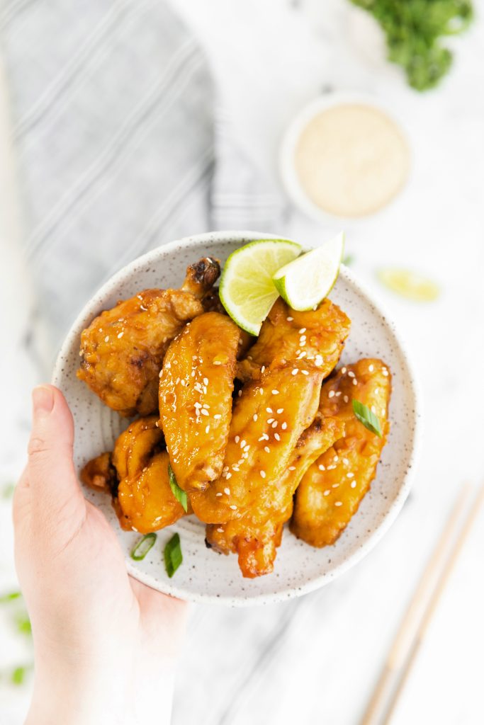 a hand holding a plate of air fryer spicy asian wings with lime wedges on the side