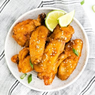 air fryer spicy asian wings on a white plate with lime wedges and sliced green onions