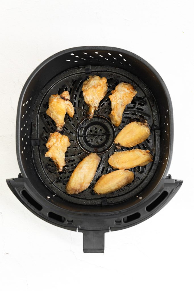golden brown chicken wings in the basket of an air fryer
